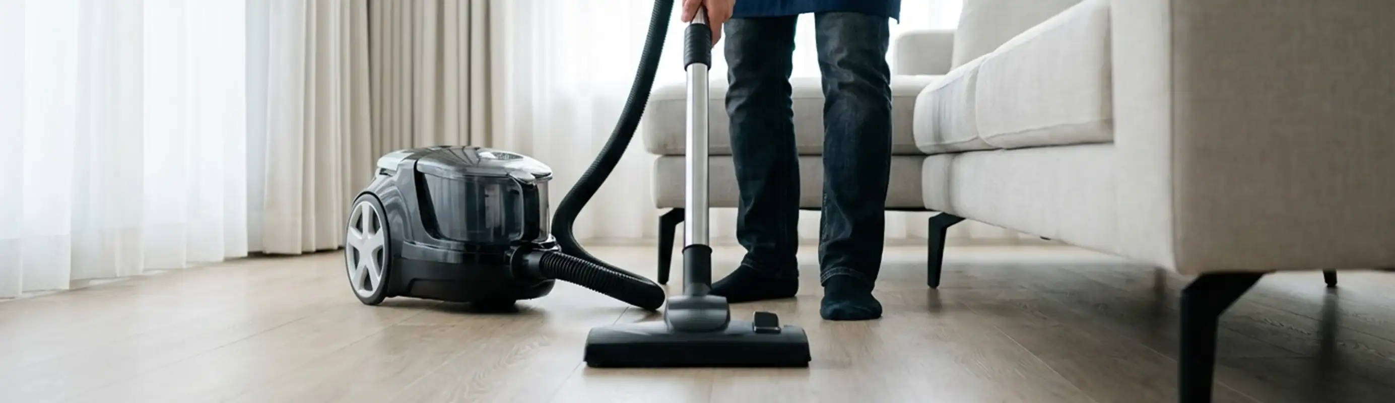 Professional house cleaner vacuuming a living room floor with a canister vacuum cleaner, Houston, TX.