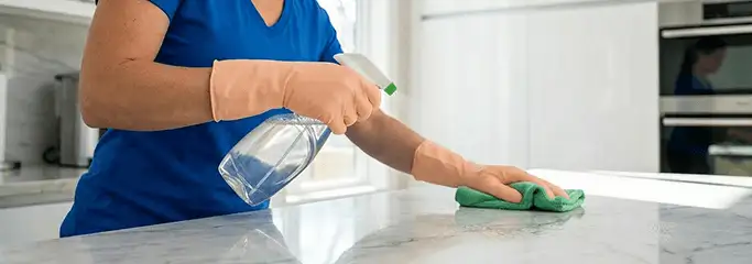 Maid service worker spraying and wiping a kitchen countertop with a microfiber cloth for sanitizing, Houston, TX.