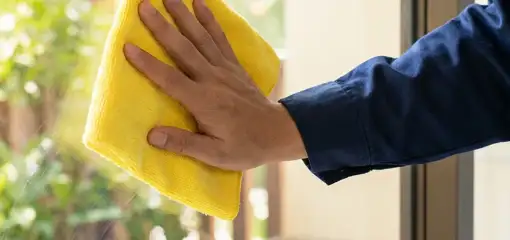 House cleaner wiping a glass window with a yellow microfiber cloth for streak-free cleaning, Houston, TX.